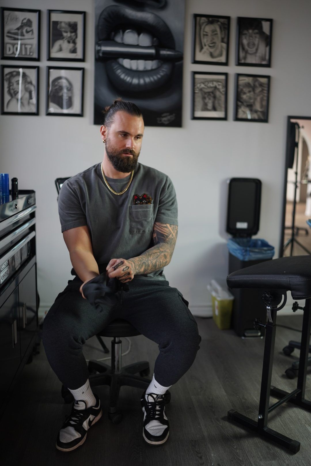 Daniel seated on a stool at his tattoo station, pulling on a black glove.