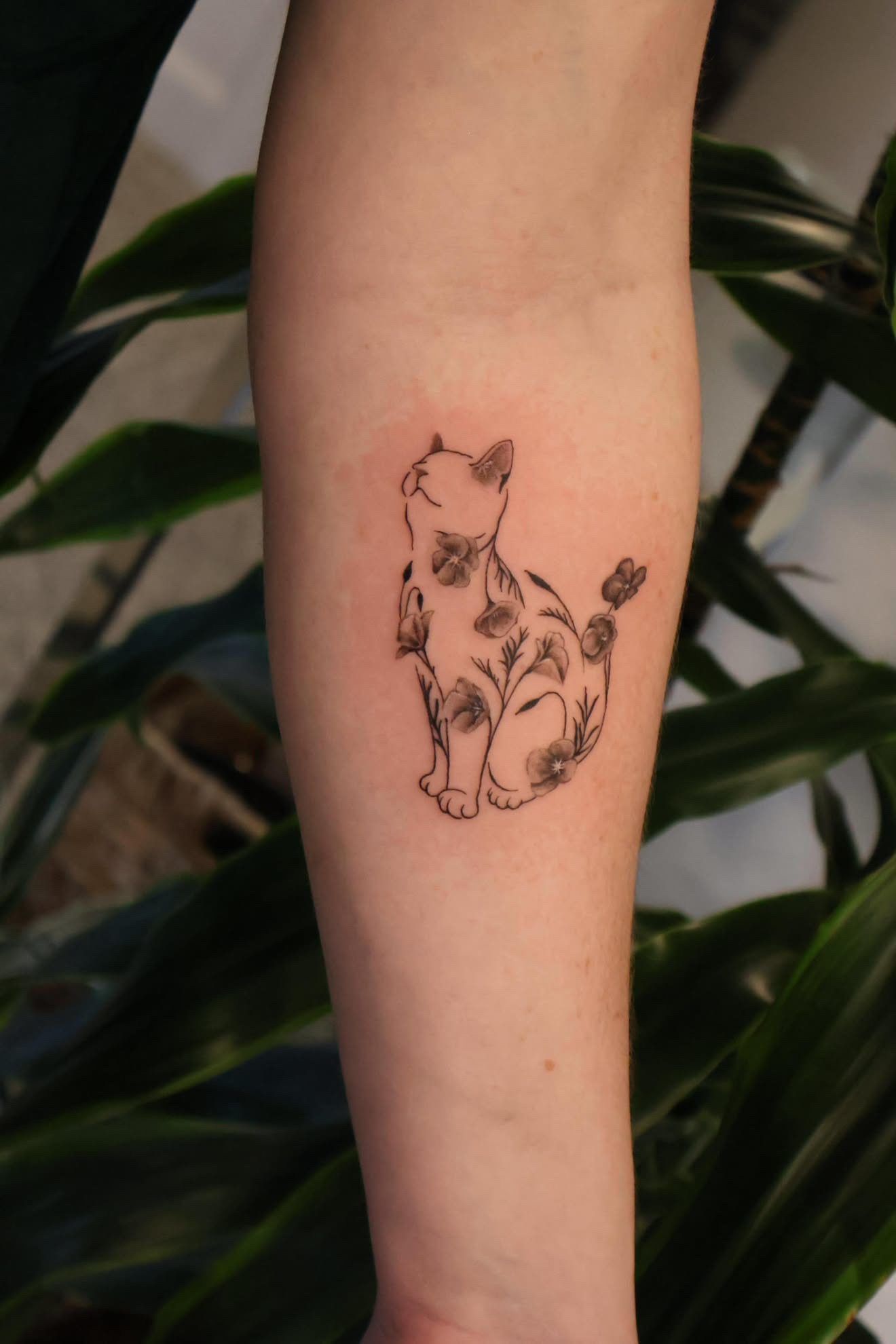 Outline of a cat filled with flowers on a forearm.