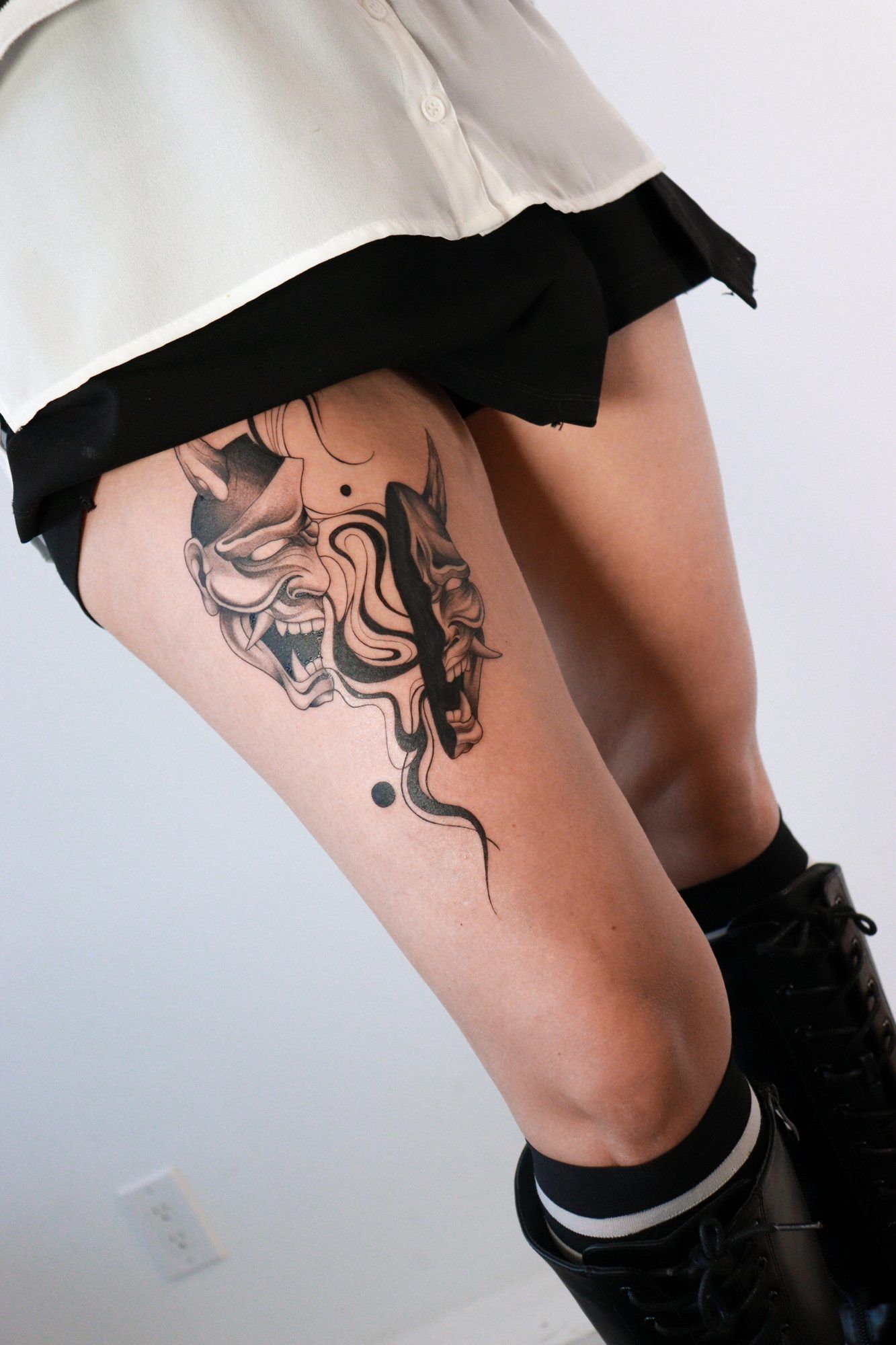Two hannya masks with flowing smoke on a woman's thigh.