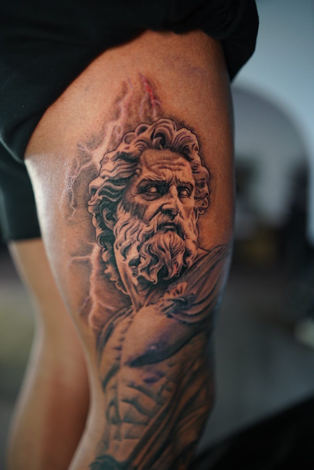Black and grey Zeus statue with lightning on a thigh.