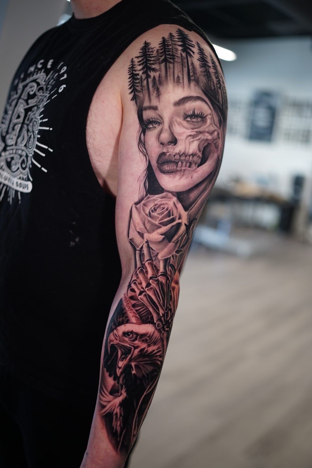 Arm sleeve with a half-skull woman under pine trees, a rose in a skeleton hand and an eagle.